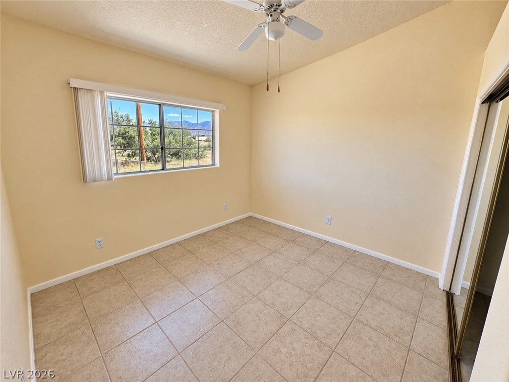 Empty bedroom with tan tile floors, a ceiling fan, and a window overlooking desert vegetation and mountains.