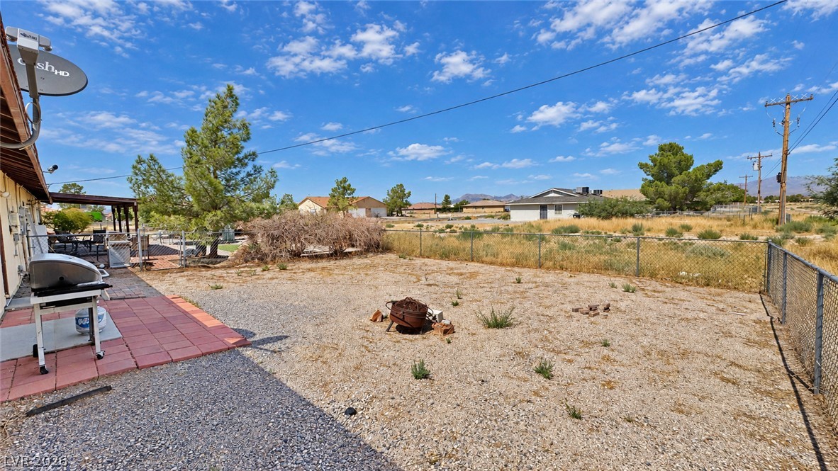 Fenced gravel backyard with a tiled barbecue patio, fire pit, and distant mountains.