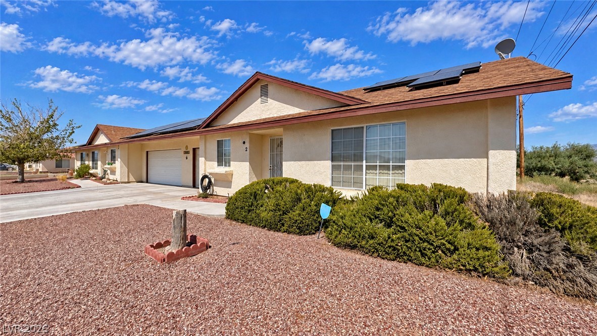 Single-story stucco home with rooftop solar panels, an attached garage, and desert landscaping.