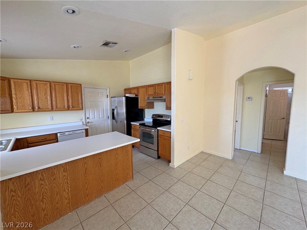 Kitchen with wood cabinets, a large white island, stainless steel appliances, and an arched hallway opening.