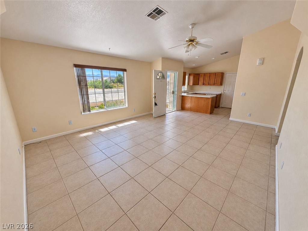 Empty tiled living area opening to a kitchen, with a ceiling fan and mountain views through the window.
