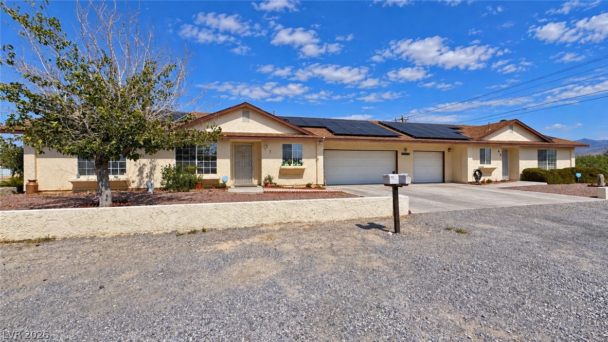 Single-story beige home with roof solar panels, multiple garages, and a gravel front yard.