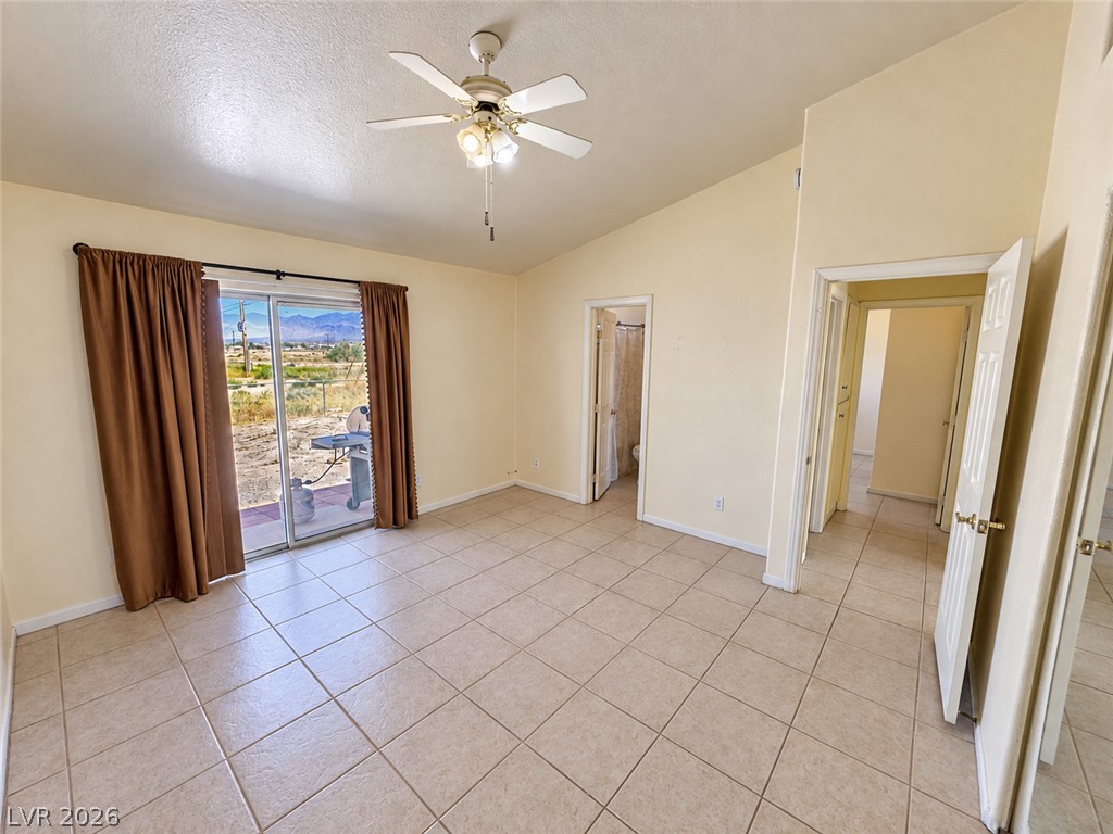 Empty tiled room with a ceiling fan, brown curtains, and a sliding glass door opening to a patio.