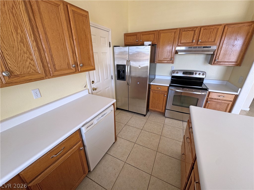 Kitchen with oak cabinets, stainless steel appliances, and beige tile flooring.
