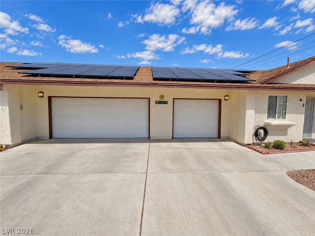 Single-story stucco home with rooftop solar panels, two garage doors, and a broad concrete driveway.