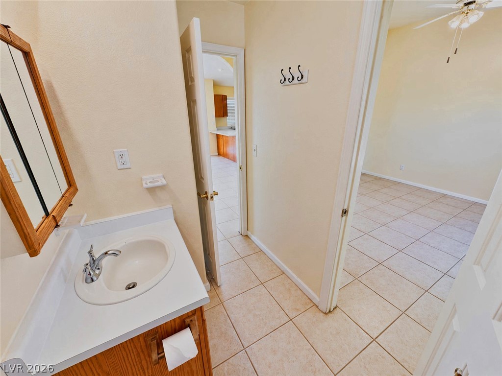 Bathroom with a white sink vanity and wood cabinetry, opening onto an empty tiled room.