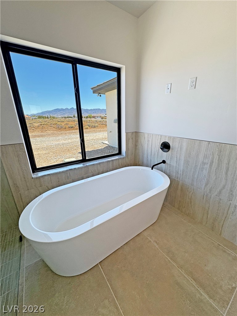 Bathroom with a freestanding white tub beneath a large window overlooking distant mountains.