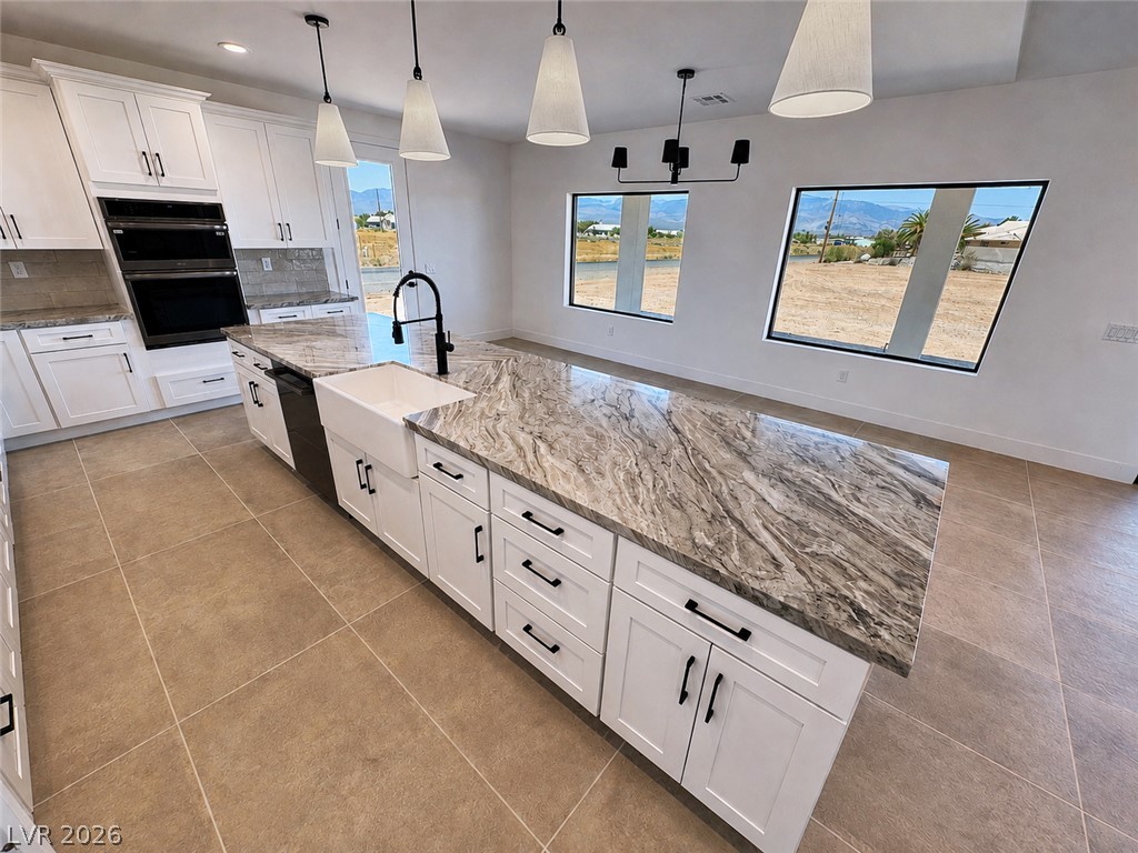 Modern kitchen with a large veined-stone island, white cabinets, and desert views through wide windows.