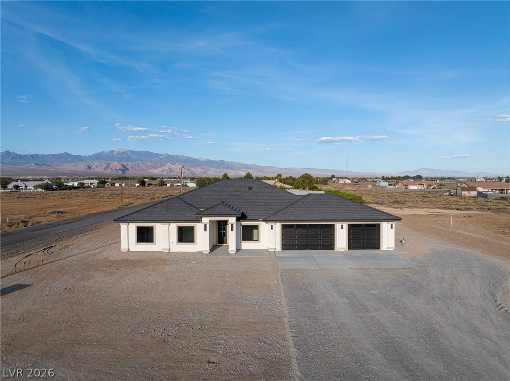 Single-story home with a dark roof and two garage doors on a gravel lot, with mountains in the distance.