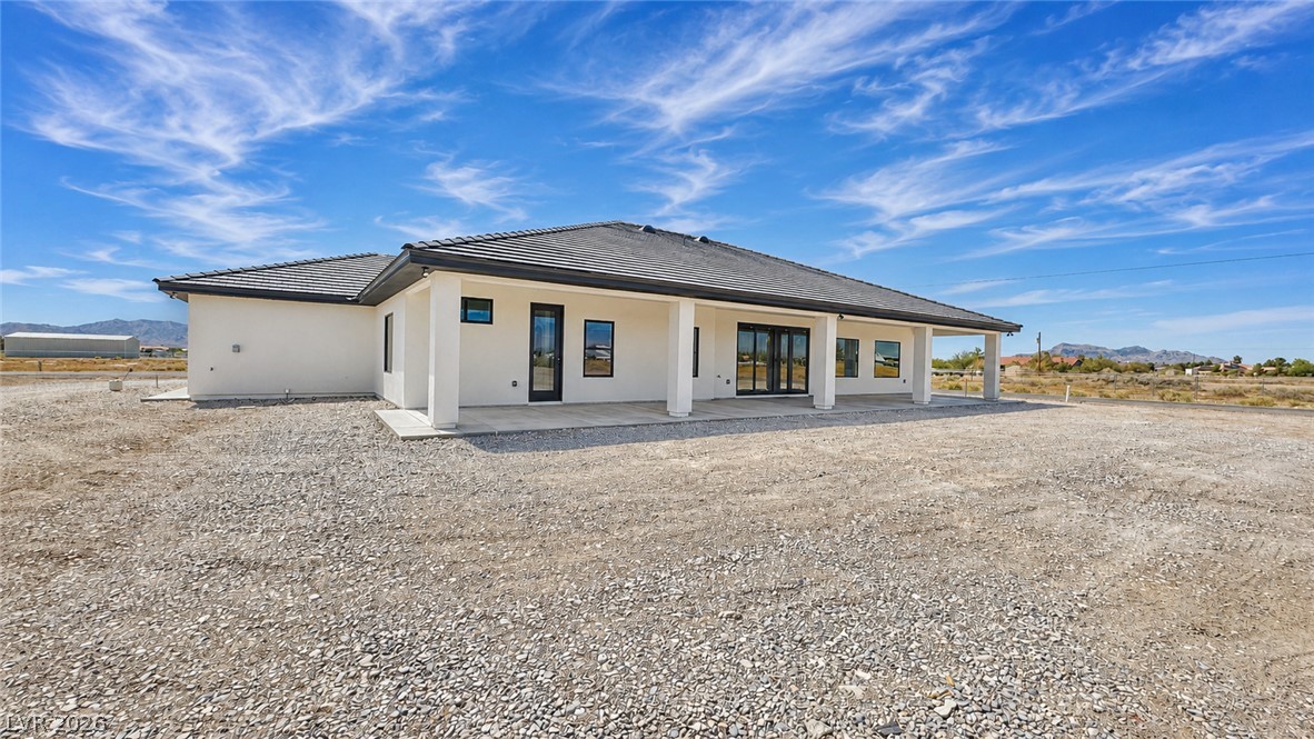 Single-story white house with a tiled roof, covered patio, gravel lot, and distant mountains.
