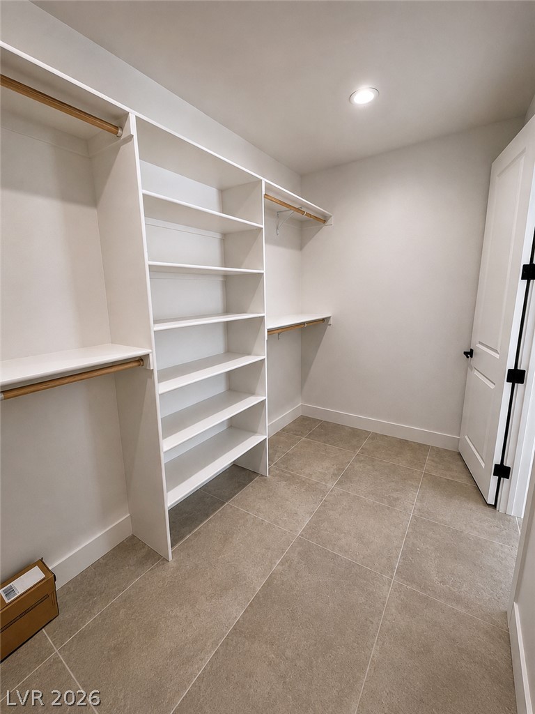 Walk-in closet with built-in shelving, wooden hanging rods, and beige tile flooring.
