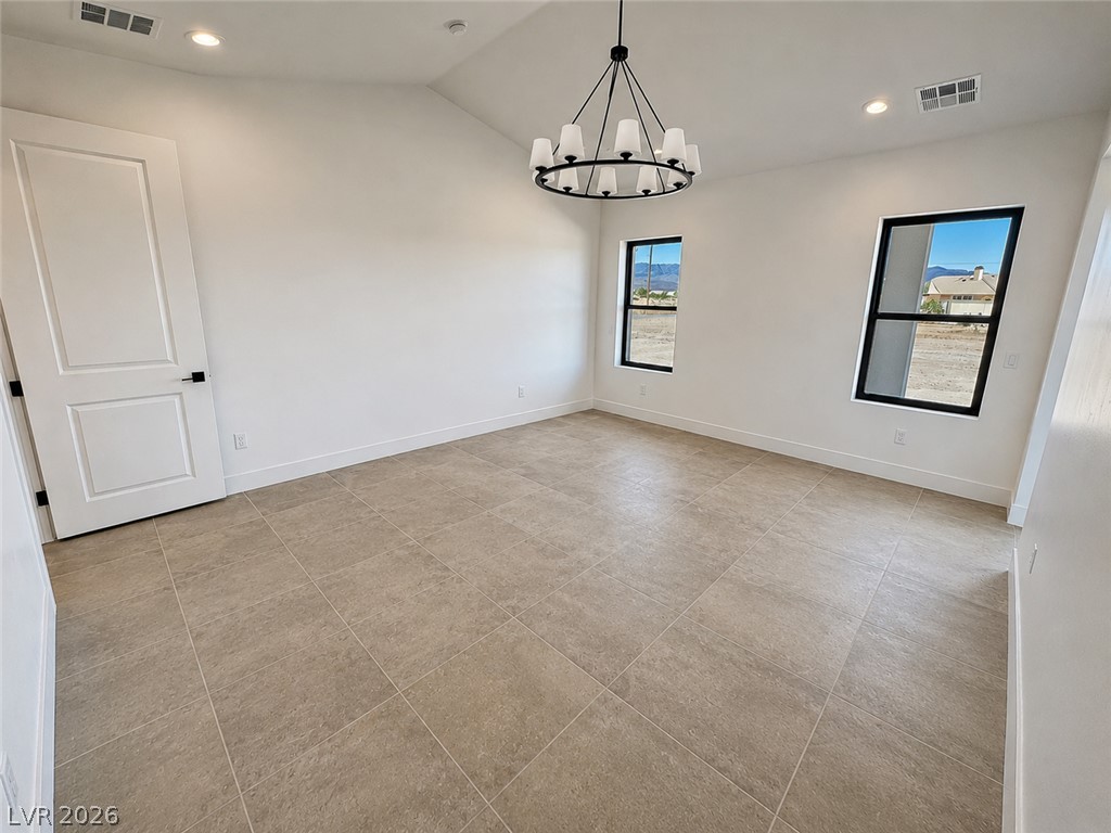 Empty dining room with beige tile flooring, a black chandelier, and mountain views through two windows.