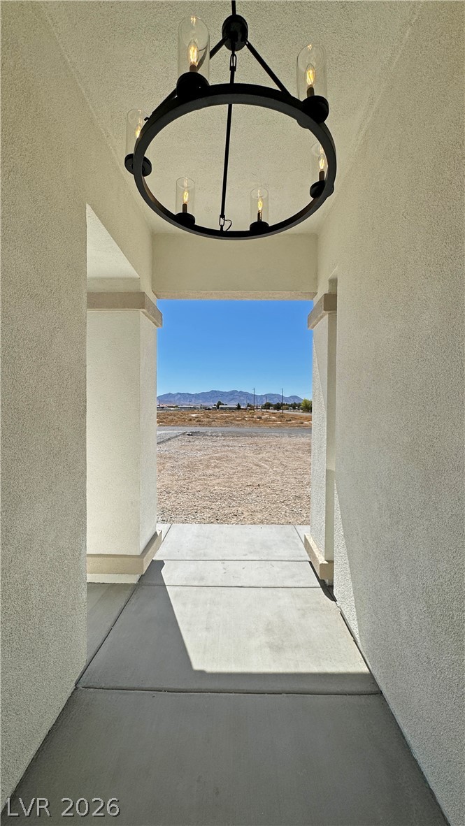 Covered stucco entry with a black circular chandelier and a view of distant mountains.