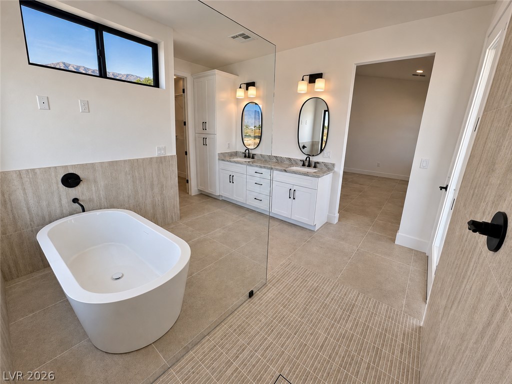 Modern bathroom with a freestanding tub, glass shower, double vanity, and high windows overlooking distant mountains.