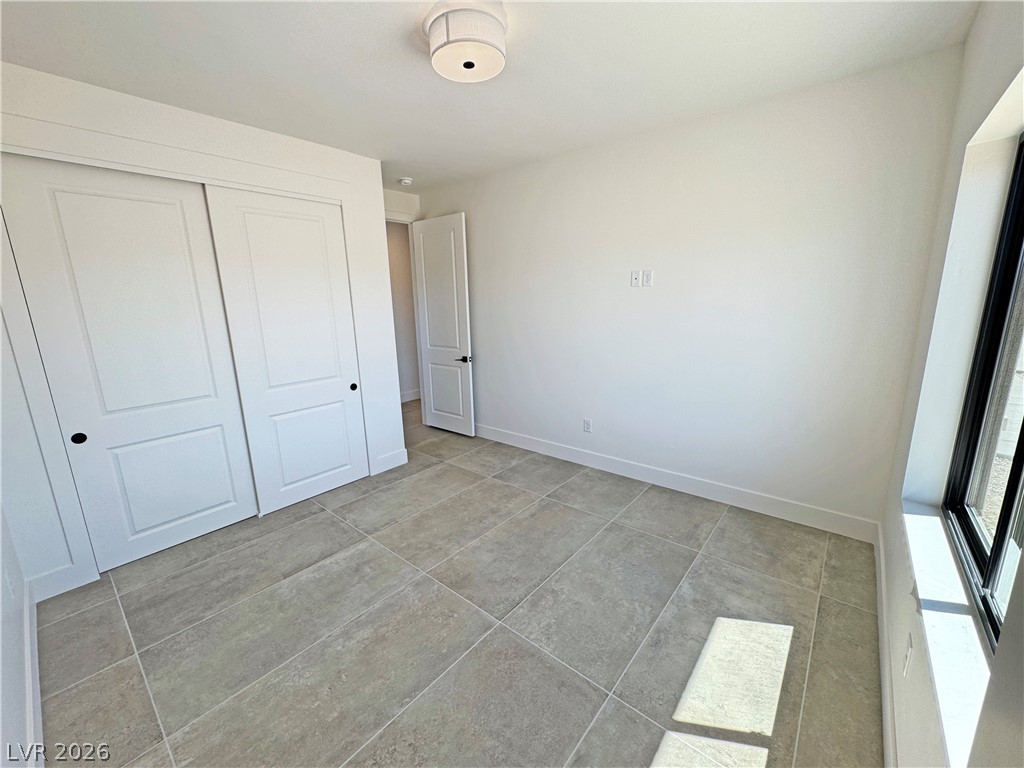 Empty room with gray tile flooring, white paneled closet doors, and a large window.