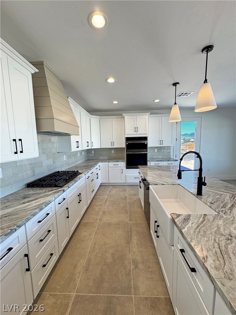 Modern kitchen with white cabinetry, veined stone island, farmhouse sink, and black faucet.