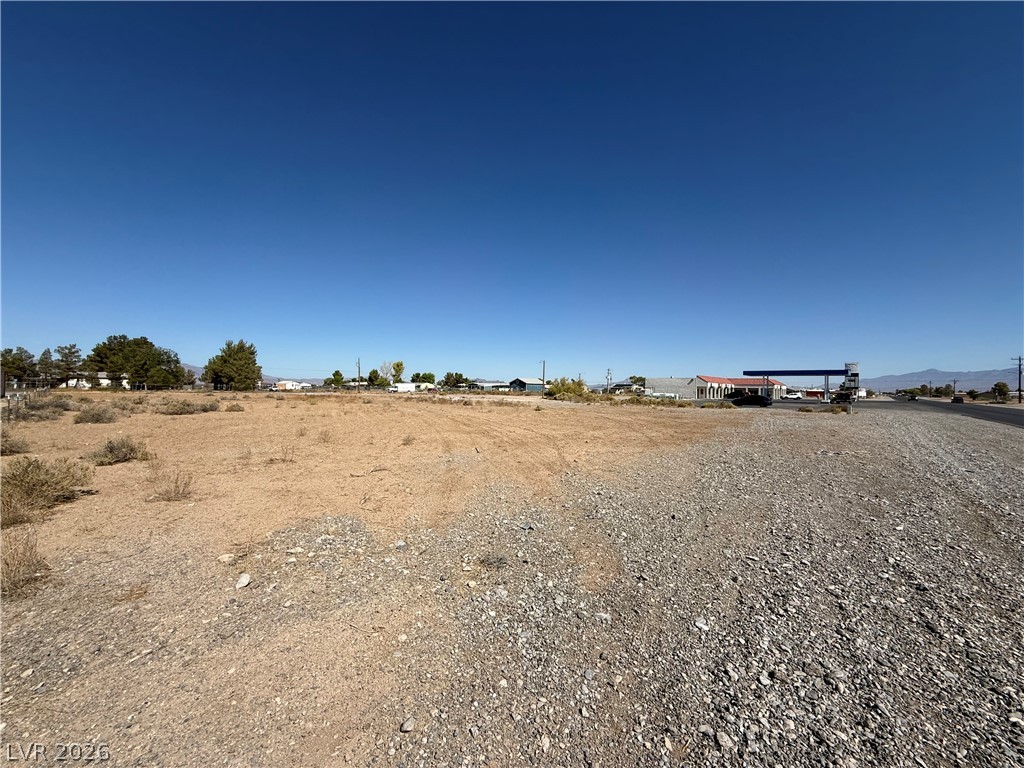 Vacant desert lot with gravel frontage, roadside buildings, and distant hills.