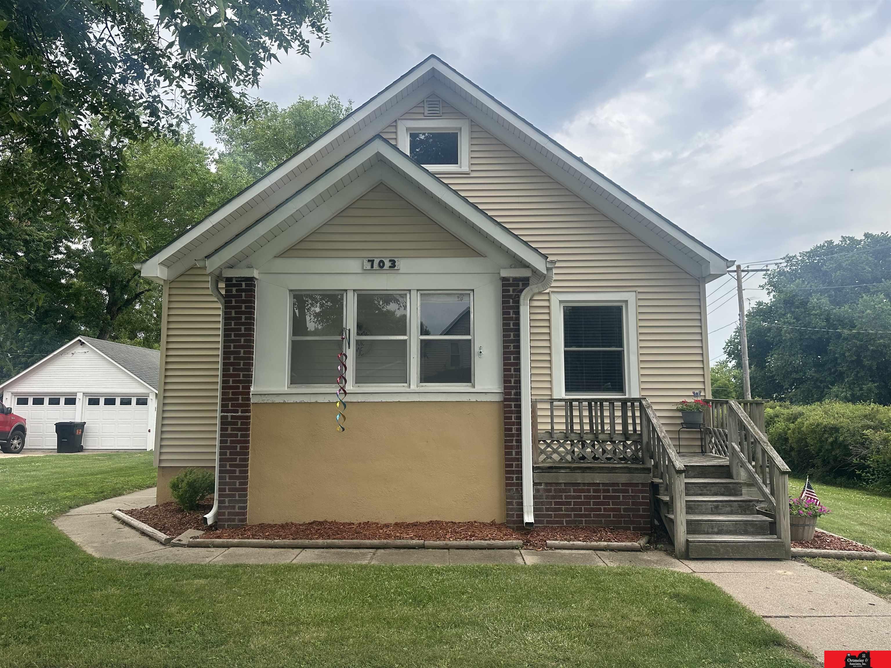 Beige gabled house with brick columns, front windows, and wooden porch stairs; house number 703 above the windows.