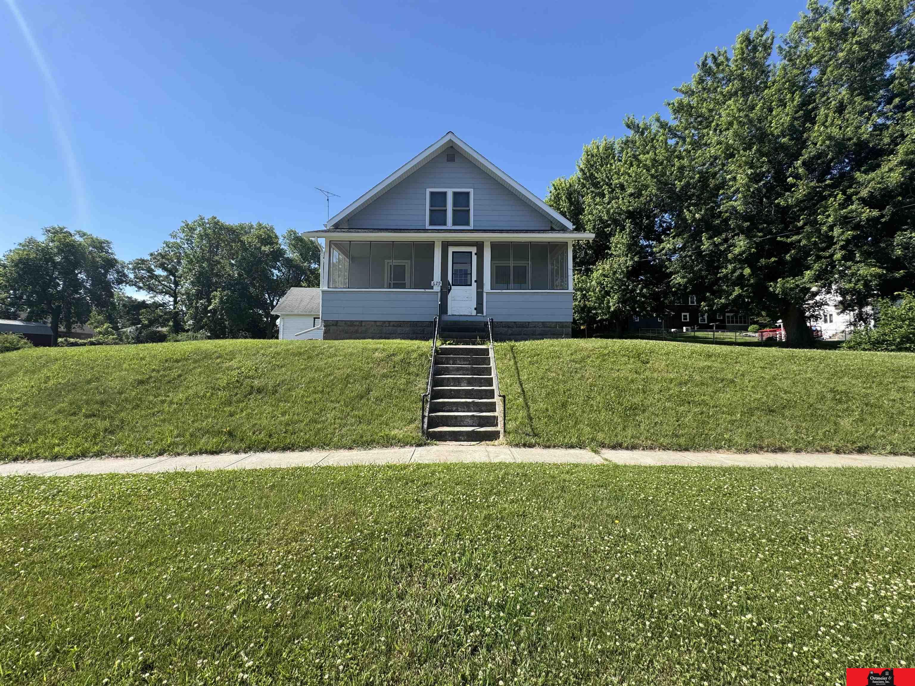 Gray-blue house with a screened porch and central steps above a broad grassy lawn.