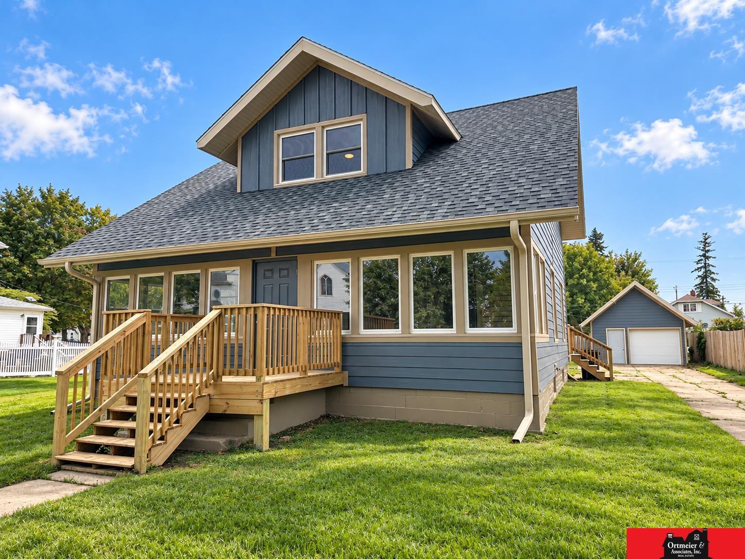 Blue-sided house with a broad wooden front porch and detached garage.