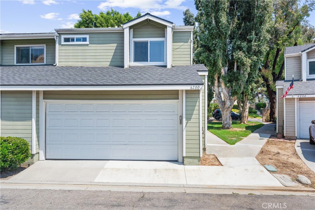 Sage-green two-story home with a white double garage door and driveway, framed by mature trees.