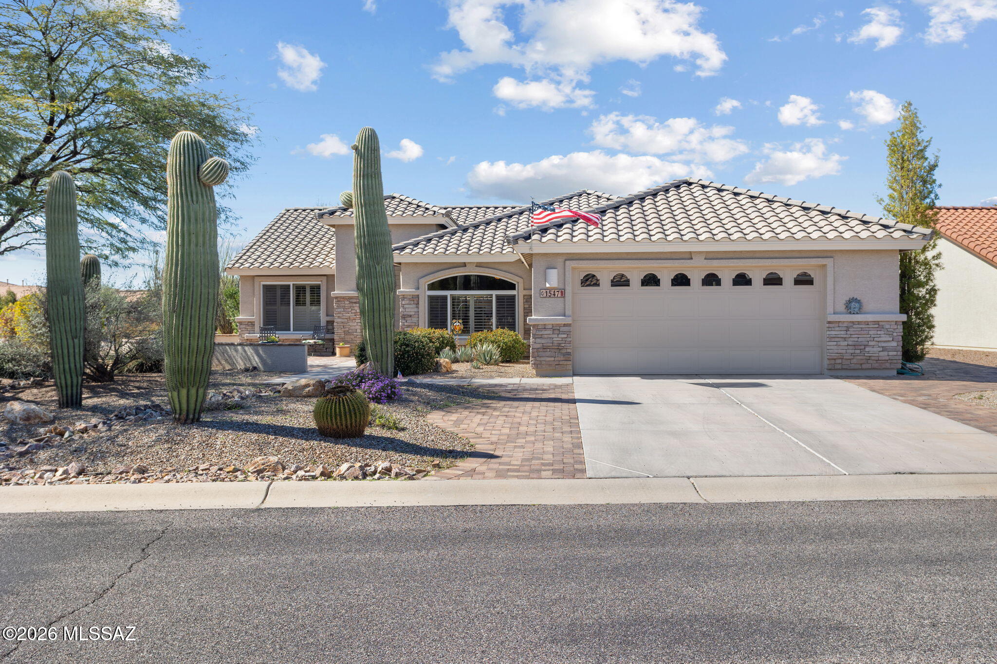 Single-story home with a tile roof, two-car garage, and tall saguaro cacti in the front yard.