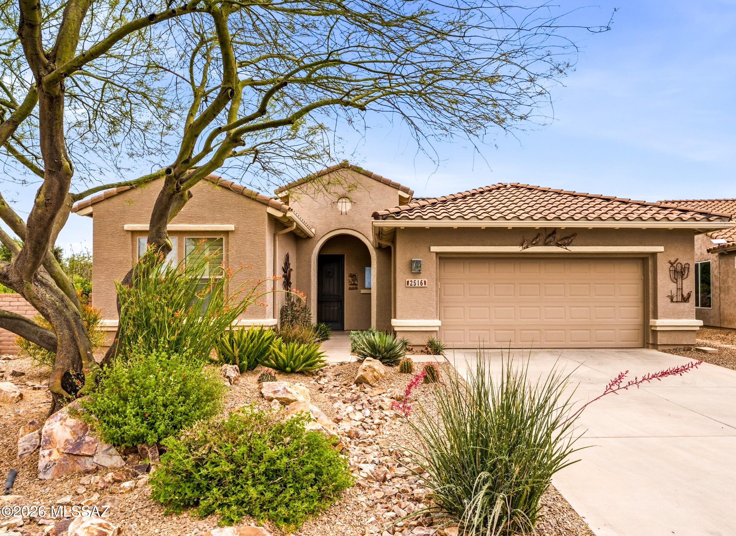 Tan stucco home with a tile roof, arched entry, two-car garage, and desert landscaping.