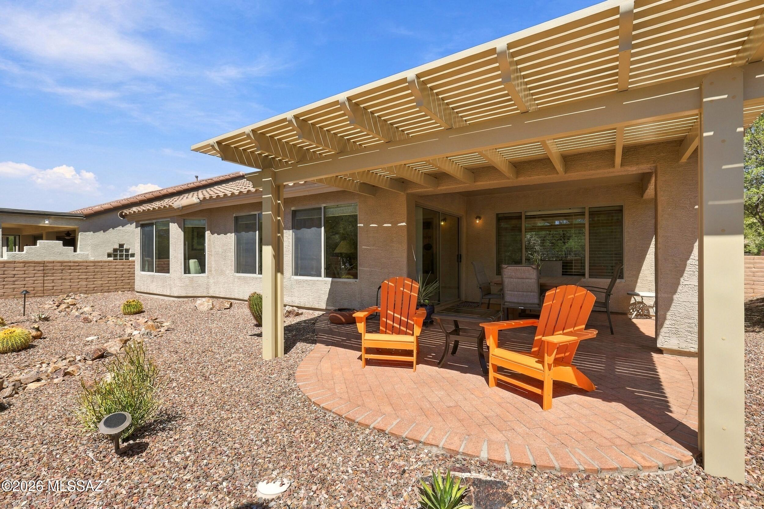 Rear patio with pergola, brick paving, orange Adirondack chairs, and desert landscaping.