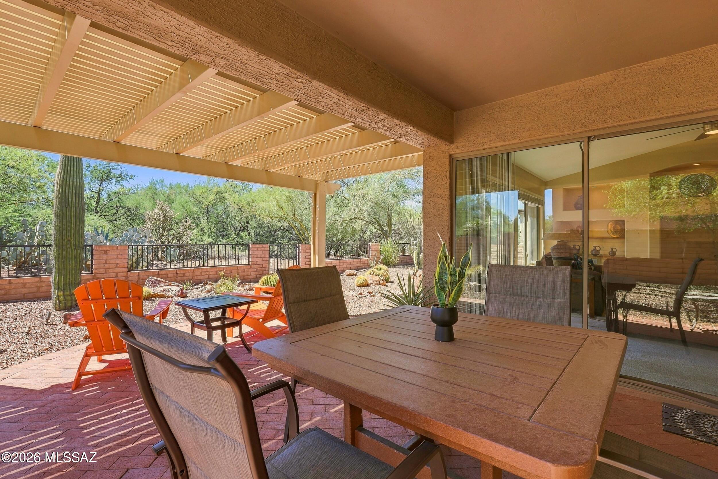Covered patio with pergola, dining table, orange chairs, and a desert garden with a tall saguaro.