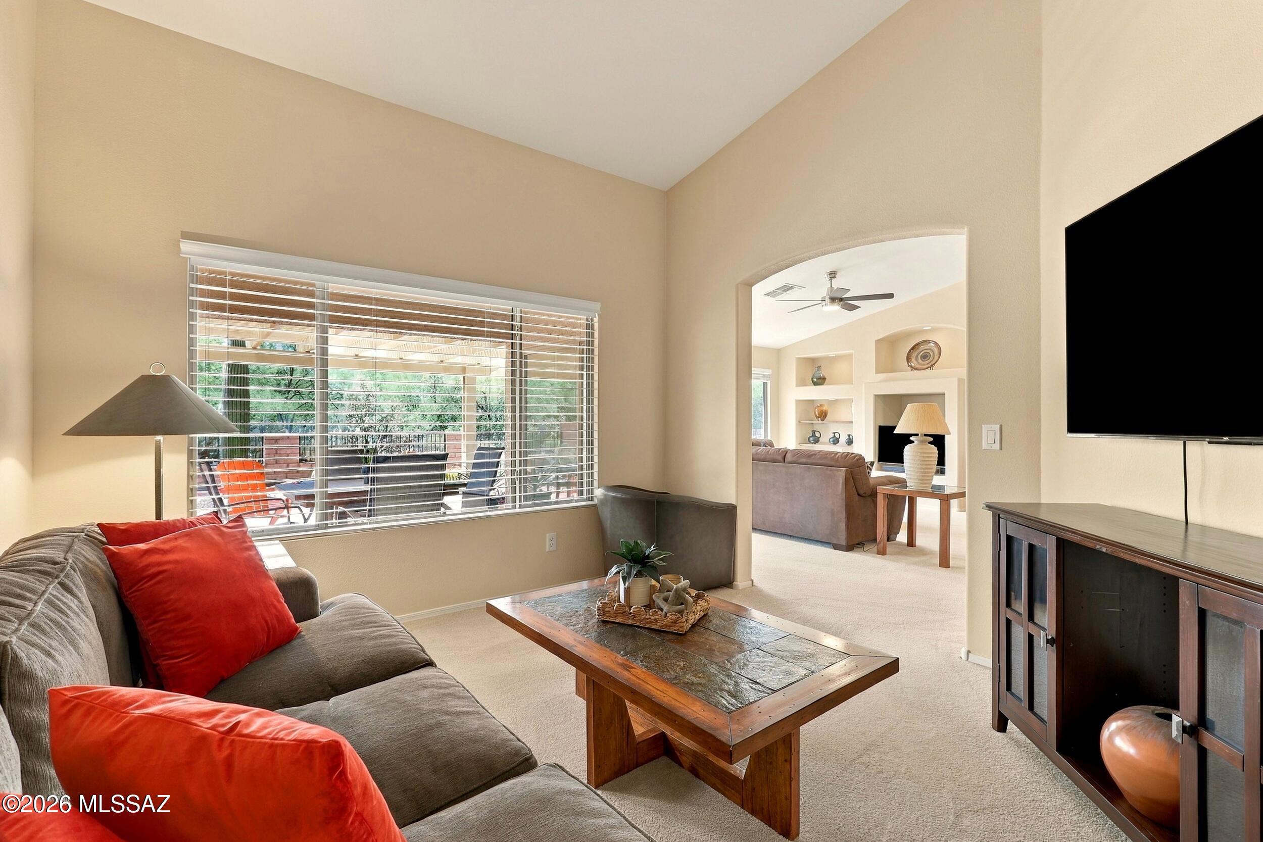 Living room with a gray sectional, red pillows, rustic coffee table, and large window facing a covered patio.