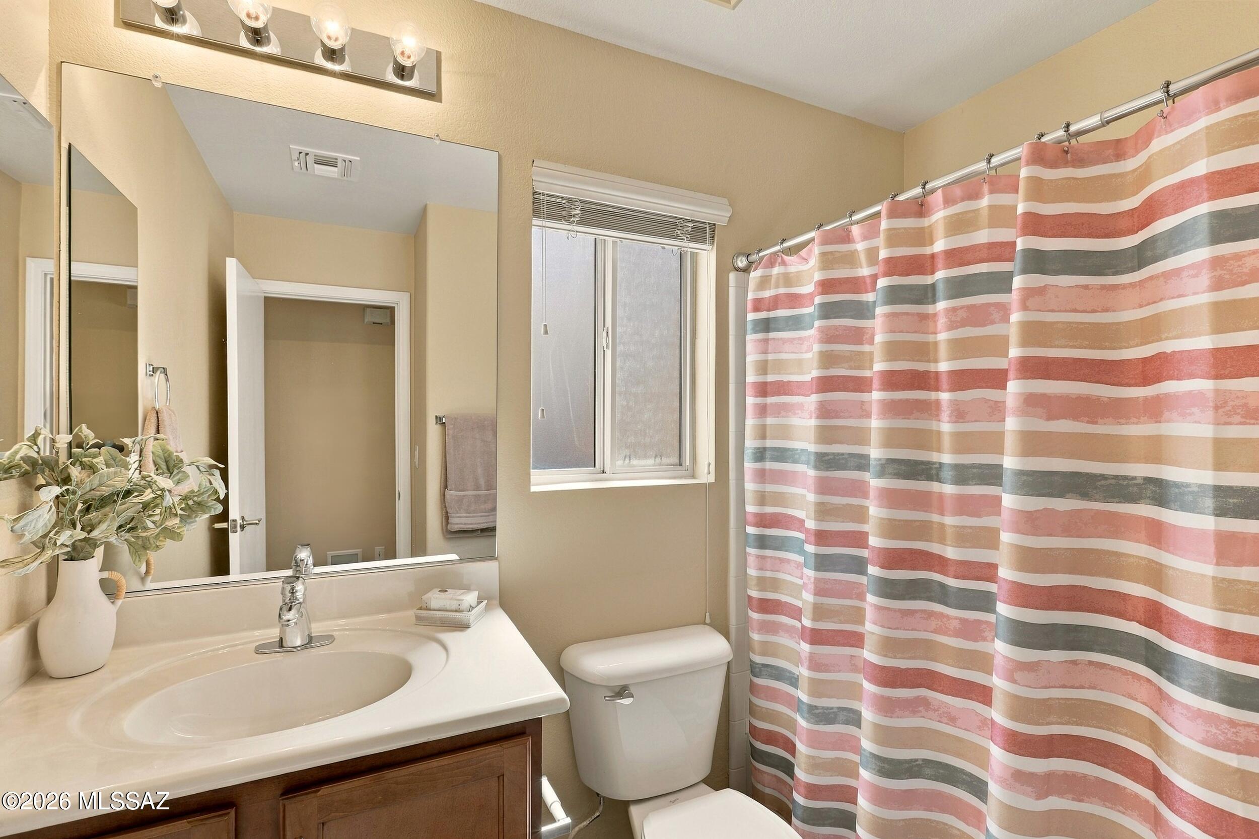 Bathroom with a large mirror, window, and pink, tan, and gray striped shower curtain.