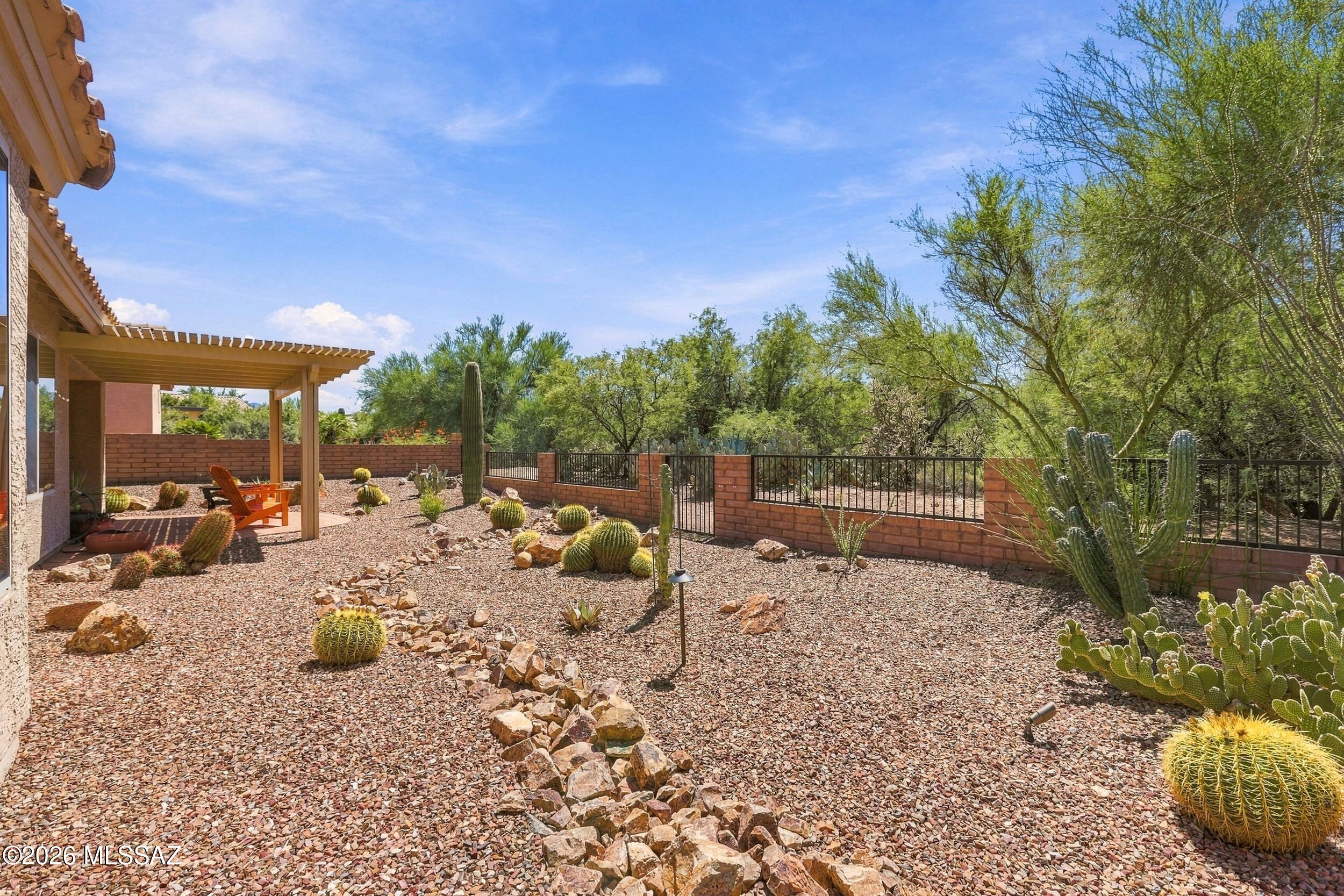 Desert backyard with gravel, cacti, and a covered patio with orange chairs.