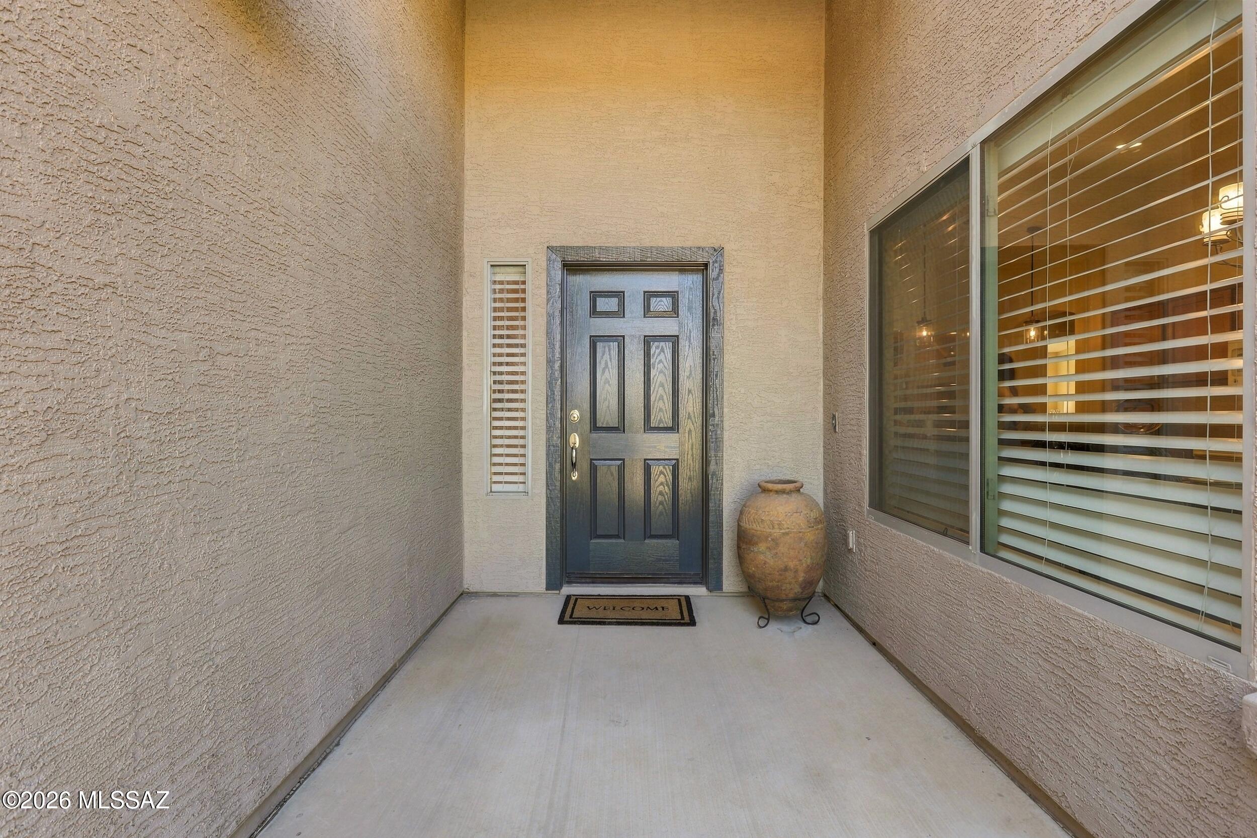 Covered home entry with a dark paneled door, large window, and decorative urn.