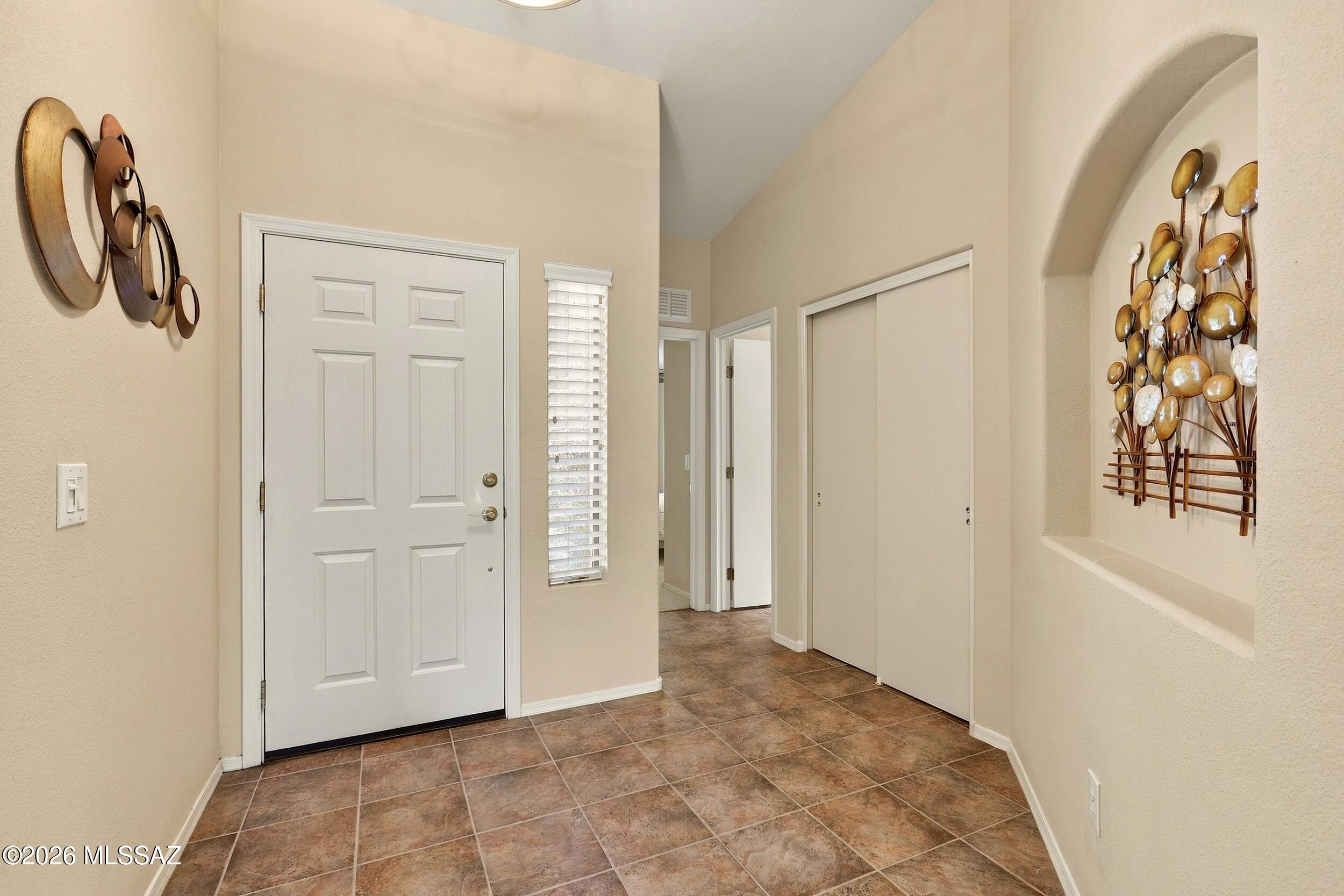 Entry foyer with brown tile flooring, a white paneled front door, and decorative art in an arched niche.