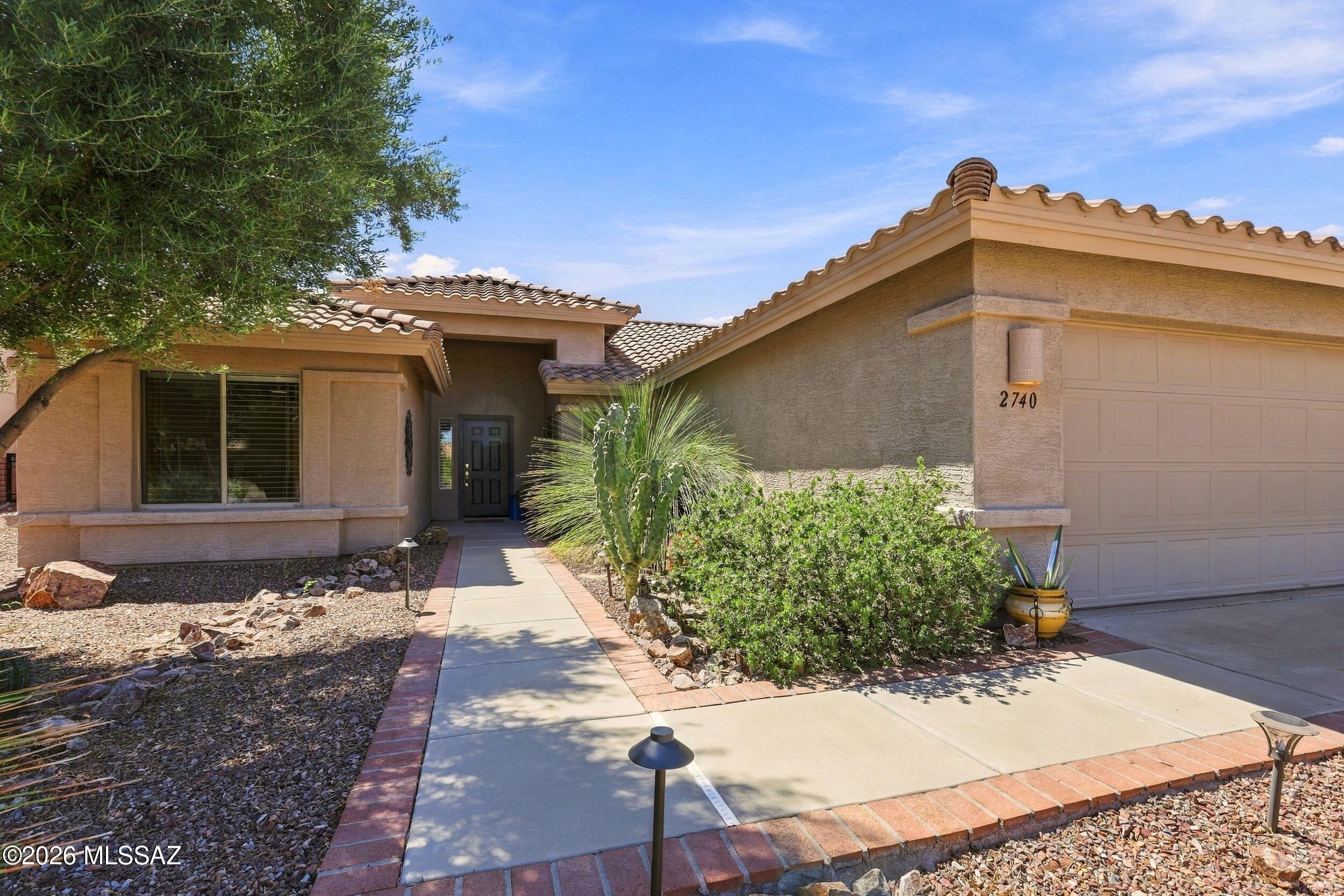 Stucco home with tile roof, attached garage, desert landscaping, and a walkway to the front door.