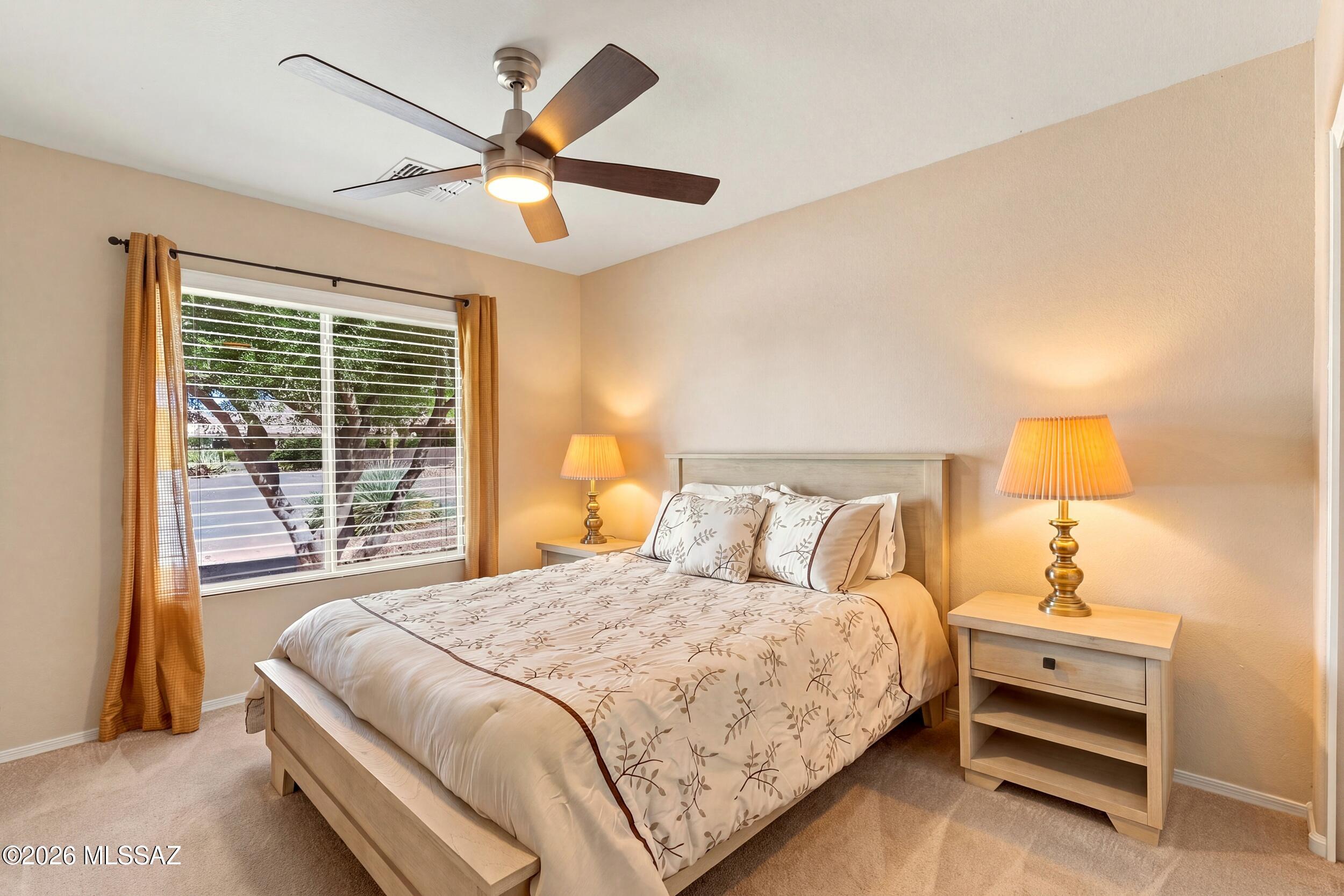 Furnished bedroom with floral bedding, matching bedside lamps, and a ceiling fan.