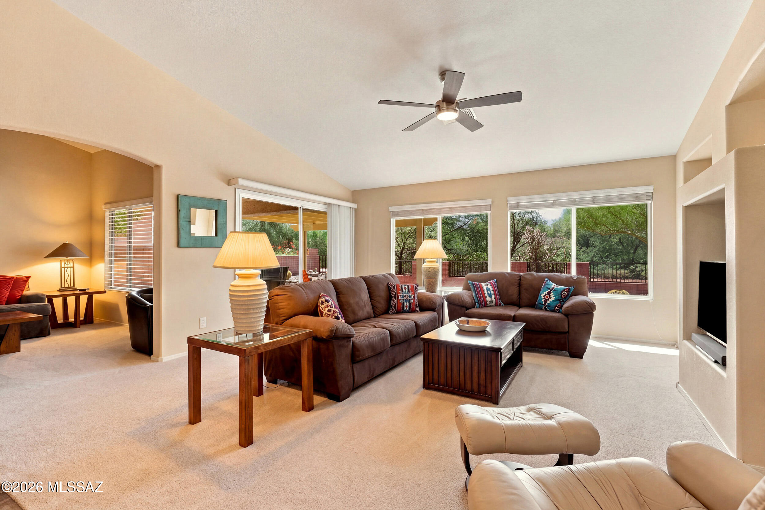 Furnished living room with brown sectional sofas, a wood coffee table, and large windows overlooking trees.