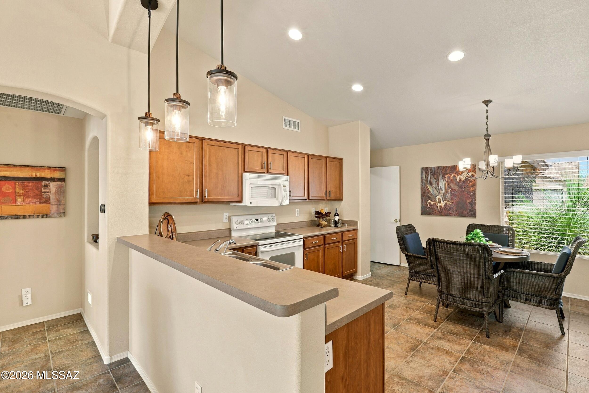 Kitchen with wood cabinets and peninsula opening to a wicker-furnished dining area beside a large window.