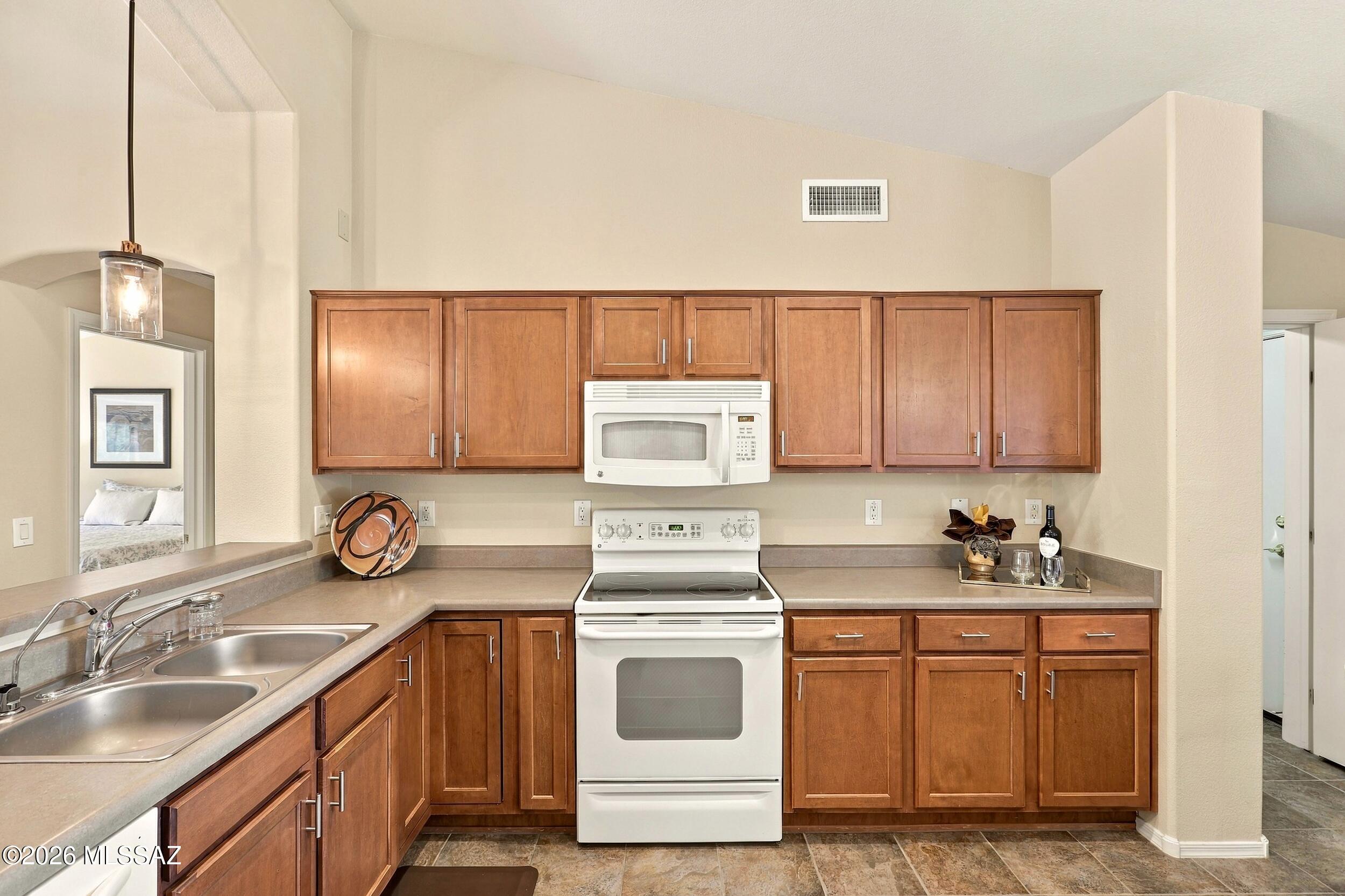 Kitchen with warm wood cabinets, a double-basin sink, and white range and microwave.