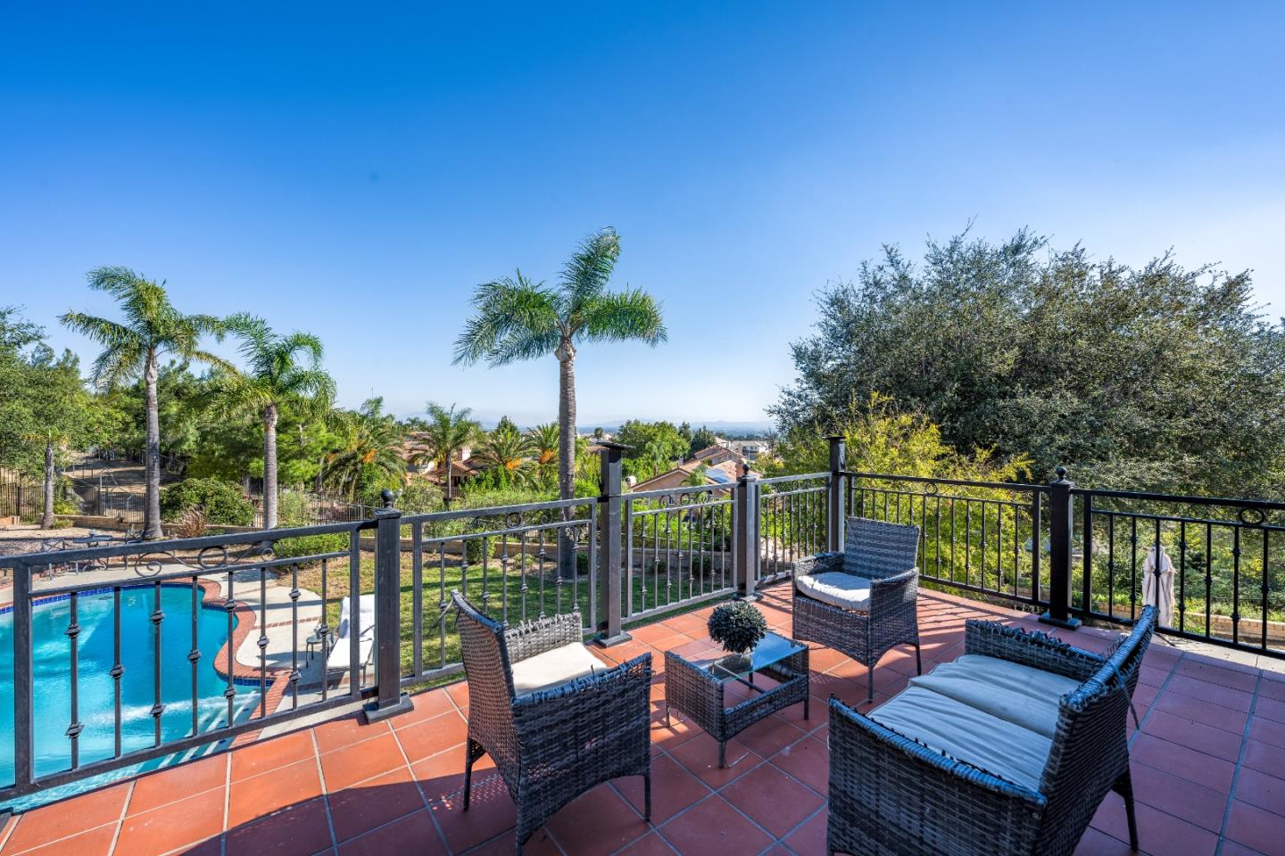 Furnished tiled terrace overlooking a pool, palm trees, and distant hills.