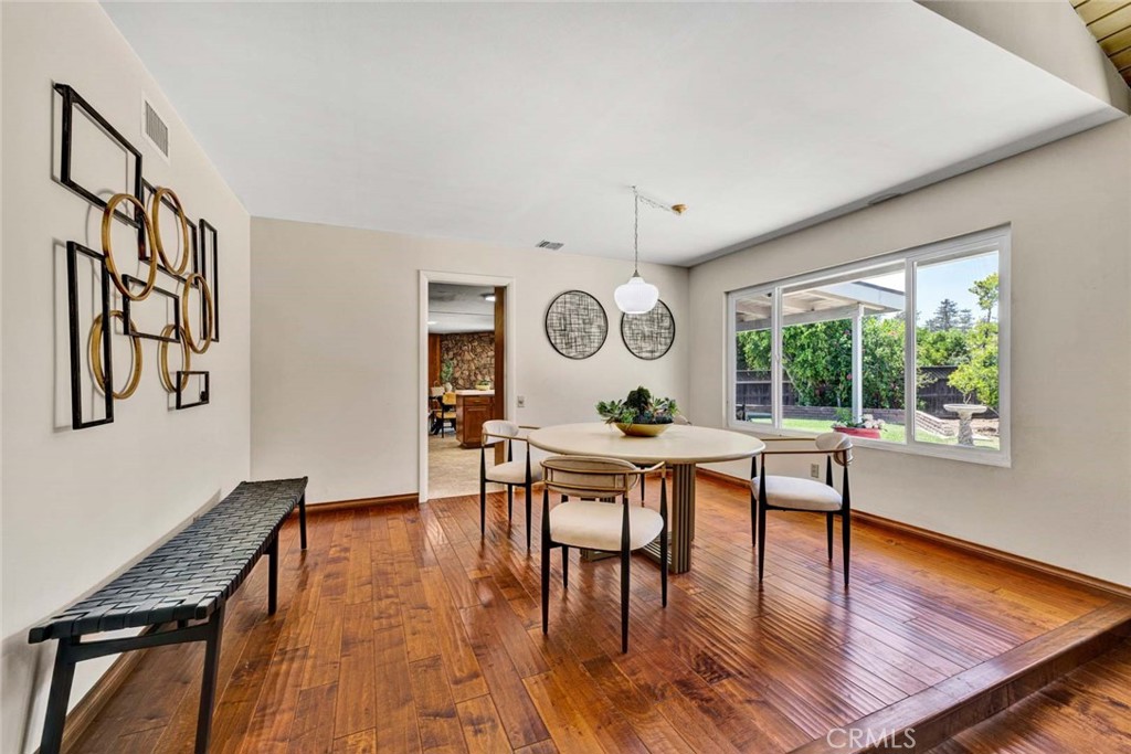 Dining room with a round table, warm wood floors, and a large window overlooking the backyard.