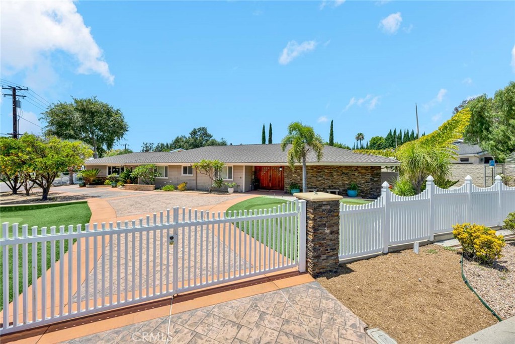 Single-story home with a stone facade and red door behind a white picket fence and gate.