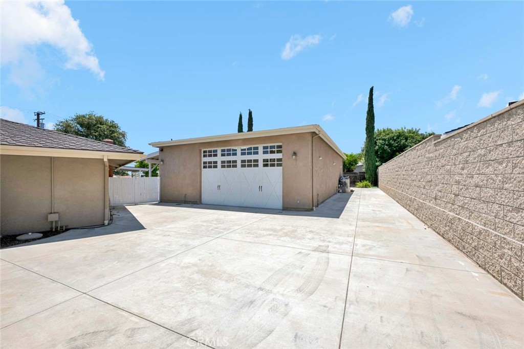 Detached garage with white double doors at the end of a wide concrete driveway beside a block wall.