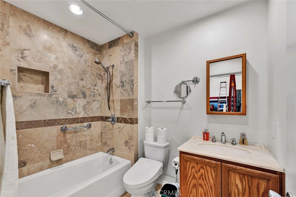 Bathroom with a stone-tile tub surround and a wood vanity with a white countertop.