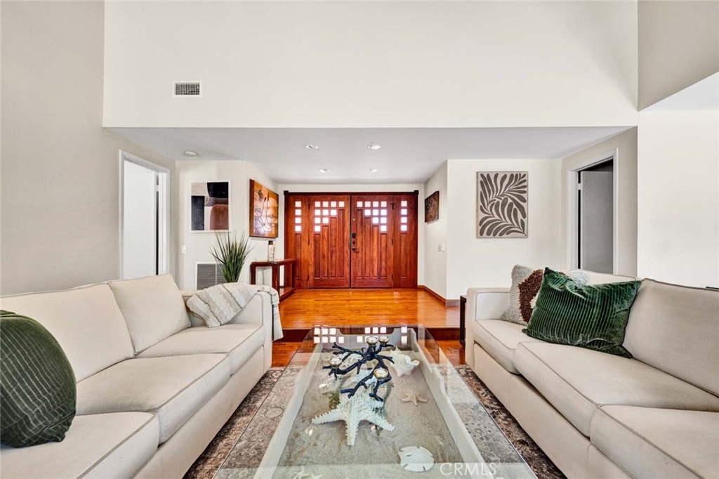 Staged living room with cream sofas and glass coffee table facing ornate wooden entry doors.