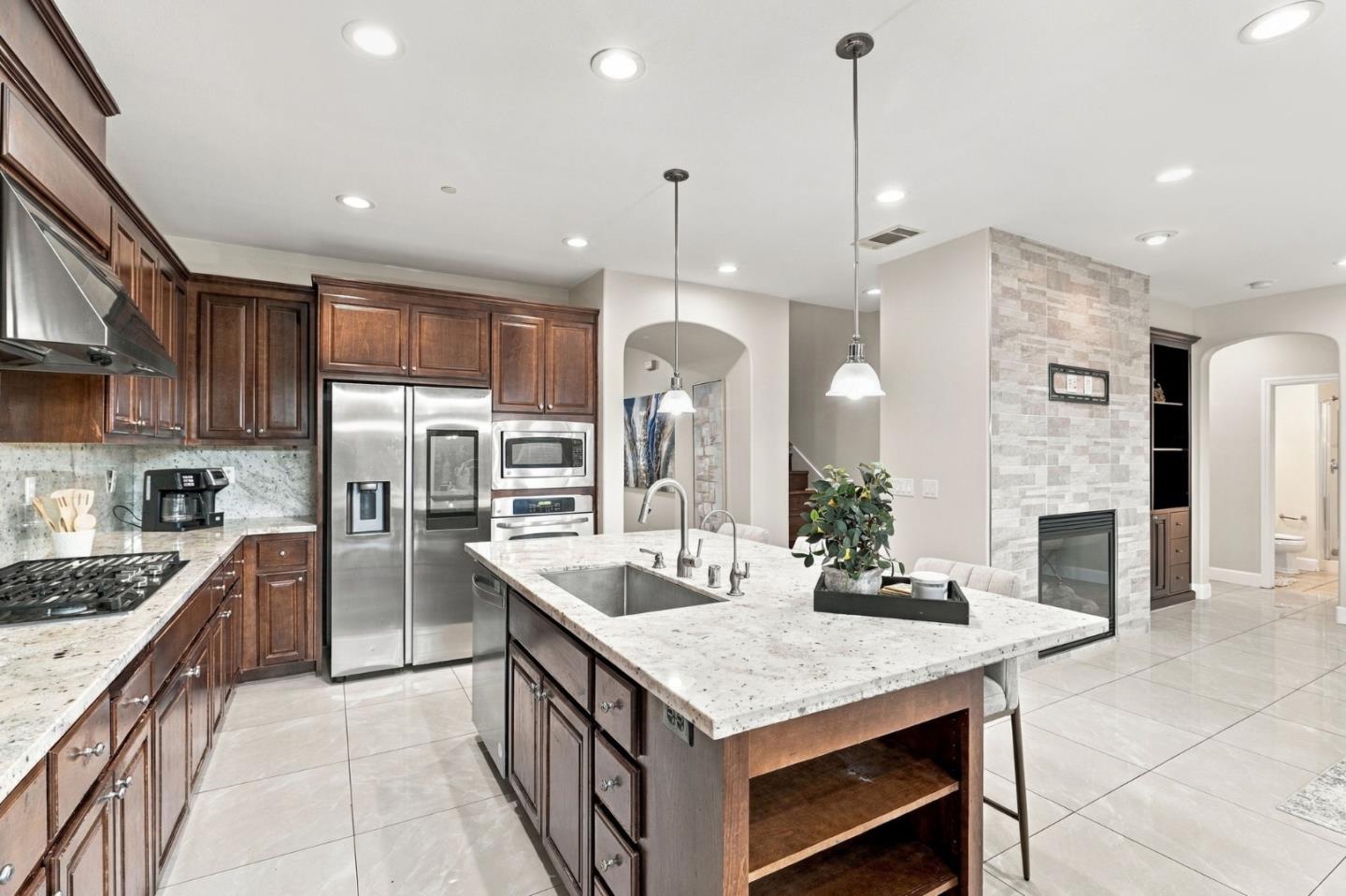 Kitchen with dark wood cabinetry, a large stone island, stainless steel appliances, and a stone fireplace.