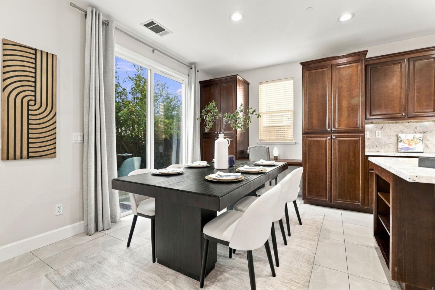 Dining area with a set dark table, white chairs, and tall dark wood kitchen cabinets.