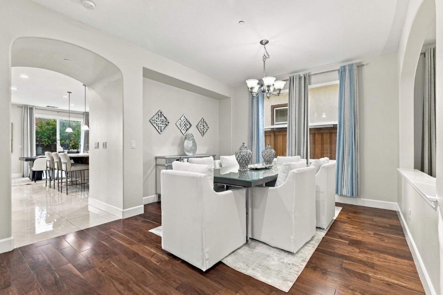 Dining room with a glass-top table, white chairs, blue curtains, and an arched opening to the kitchen.