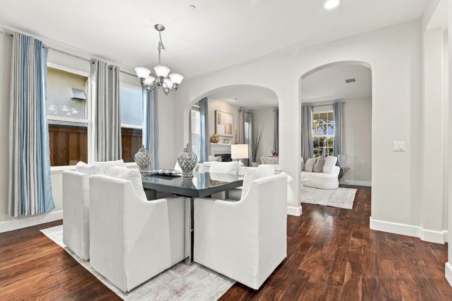 Staged dining room with white chairs, a glass-top table, hardwood floors, and arched openings to living areas.