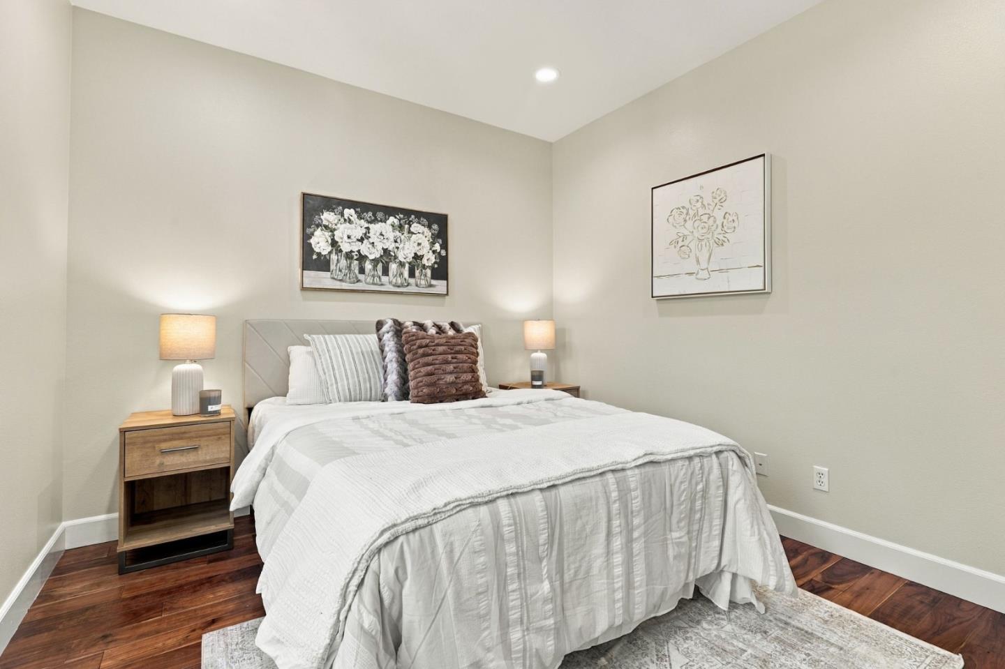 Furnished bedroom with a white quilted bed, gray headboard, bedside lamps, and floral artwork.